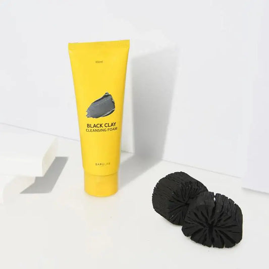 Yellow tube of Black Clay Cleansing Foam with charcoal scrub pads on white background