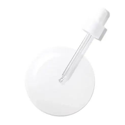 Clear glass dropper with white cap dispensing serum onto white surface, minimalist skincare product
