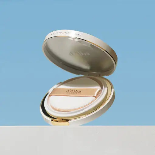 d'Alba White Truffle cushion compact with gold accents, open against soft blue background