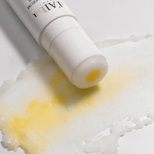 Yellow serum droplet from white tube on textured surface, showcasing skincare product texture and application