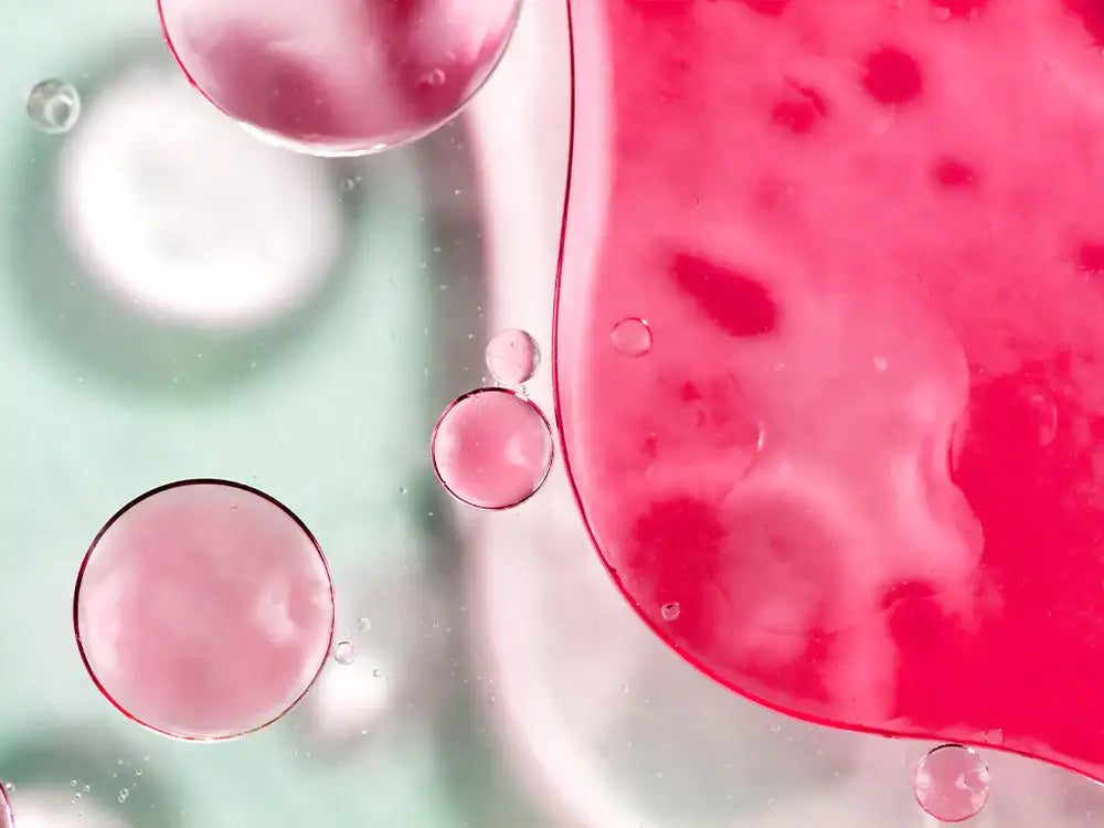 Pink and clear oil bubbles in liquid, showcasing skincare essence texture for radiant wellness routines