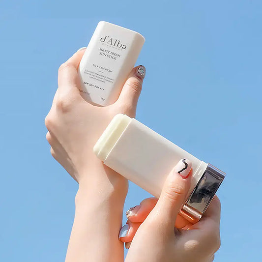 d'Alba Air Fit Fresh Sun Stick SPF 50+ PA++++ held in hands against blue sky, silky & fresh texture