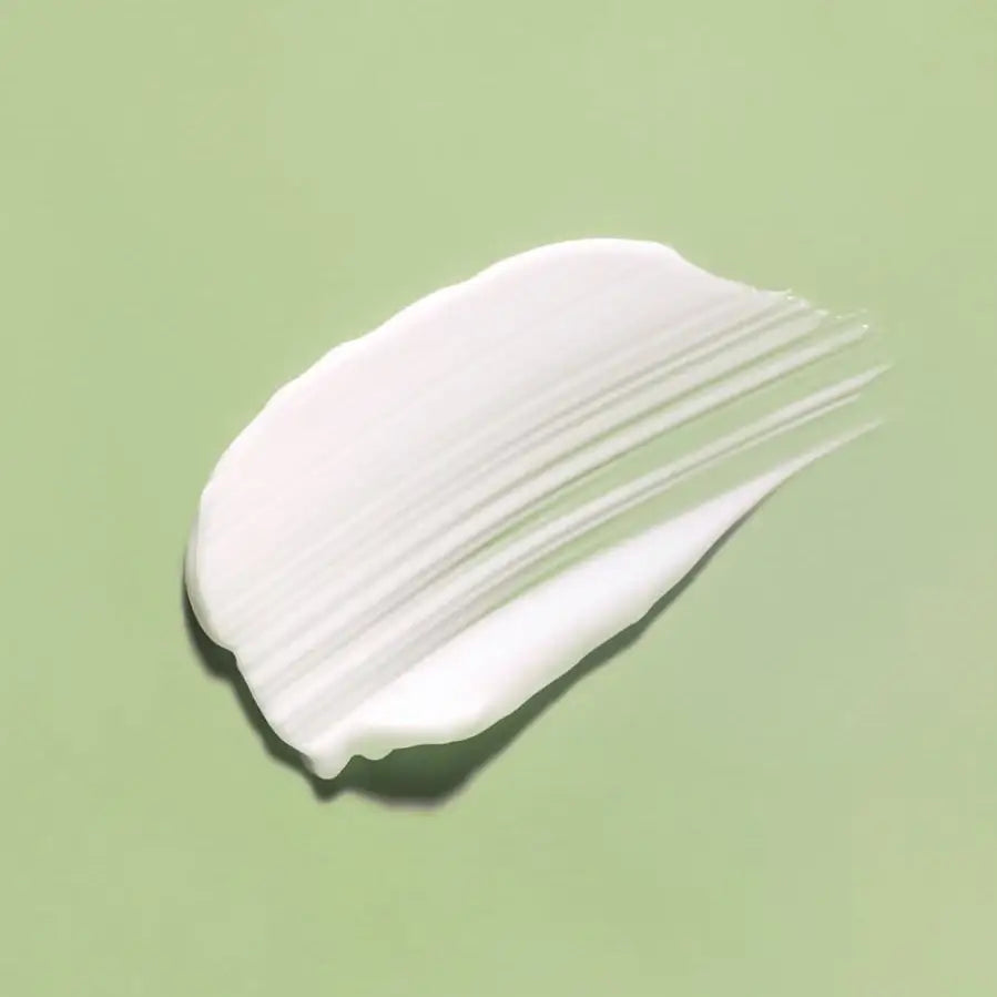 Smooth white skincare cream swatch on soft green background, showcasing creamy texture for radiant skin